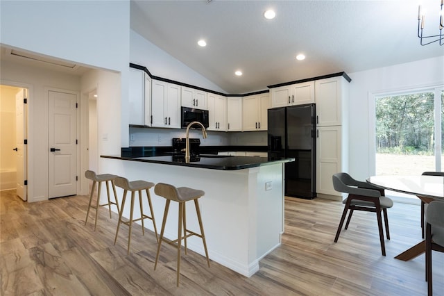kitchen featuring black appliances, a peninsula, dark countertops, vaulted ceiling, and light wood-style flooring