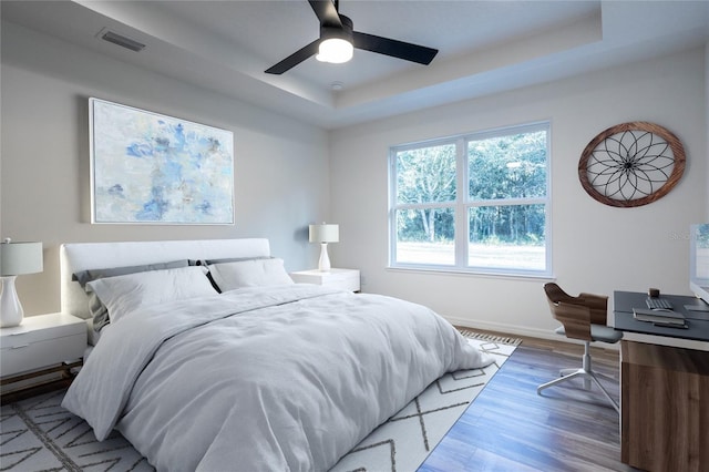 bedroom featuring a tray ceiling, wood finished floors, baseboards, and a ceiling fan