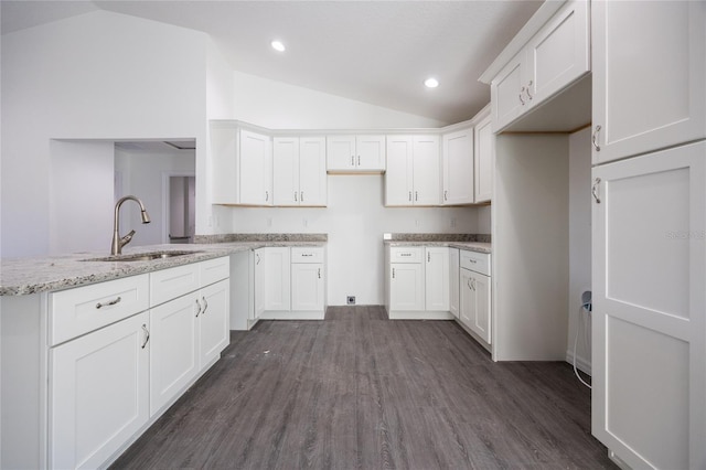 kitchen with a sink, lofted ceiling, light stone counters, dark wood-type flooring, and white cabinets