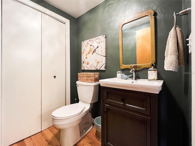 half bathroom featuring wood finished floors, toilet, and vanity