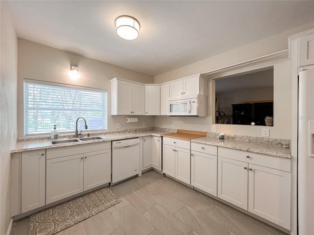 kitchen featuring a sink, white appliances, white cabinets, and light stone finish flooring