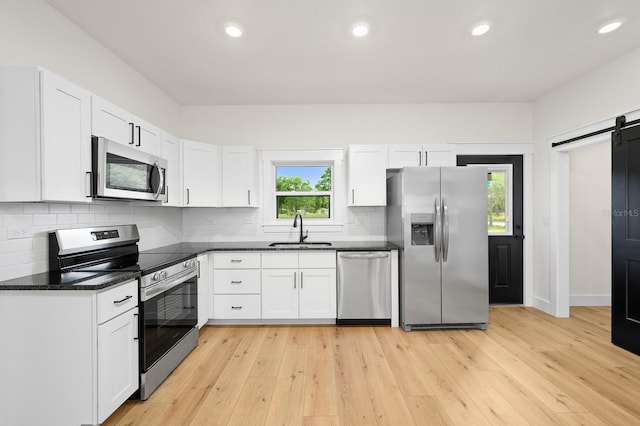 kitchen with appliances with stainless steel finishes, a sink, a barn door, dark countertops, and white cabinets