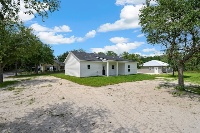 back of house with dirt driveway and a lawn