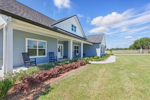 view of front of home featuring covered porch, a shingled roof, a front yard, and board and batten siding