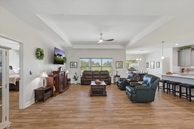 living area featuring light wood-style flooring, a raised ceiling, a ceiling fan, baseboards, and recessed lighting