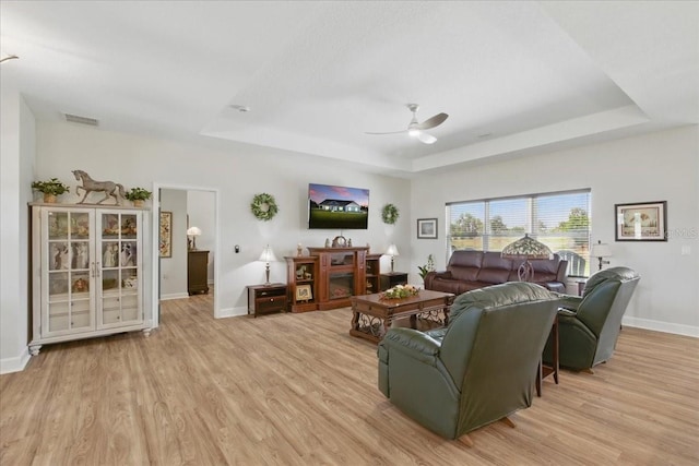 living room featuring a raised ceiling, a ceiling fan, light wood-style flooring, and baseboards