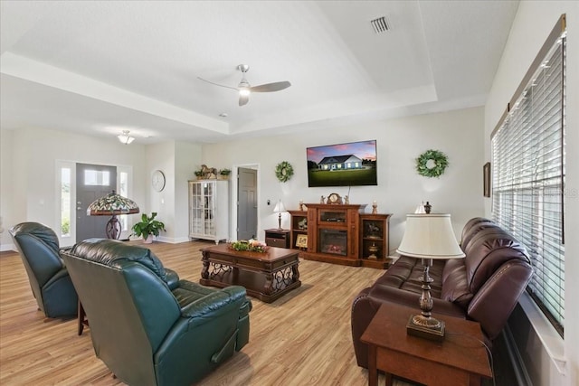 living room with a tray ceiling, light wood-style flooring, a ceiling fan, and baseboards