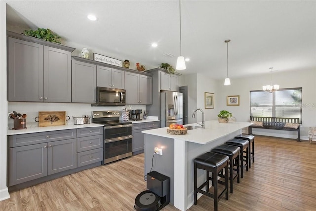 kitchen featuring stainless steel appliances, a sink, gray cabinets, a breakfast bar area, and light wood-type flooring