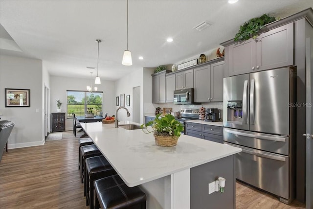 kitchen featuring appliances with stainless steel finishes, a sink, gray cabinets, a breakfast bar, and recessed lighting