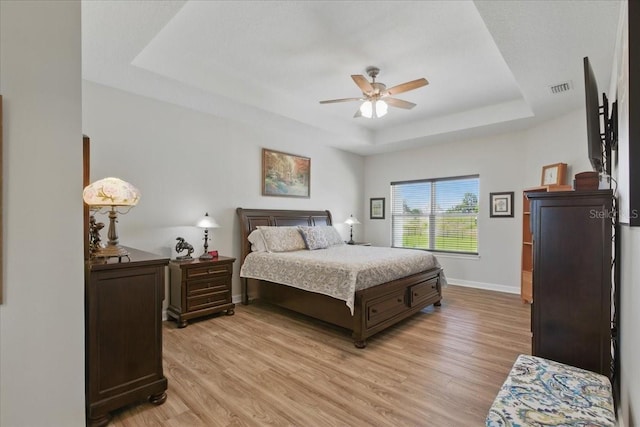 bedroom featuring a tray ceiling, light wood-style flooring, baseboards, and ceiling fan