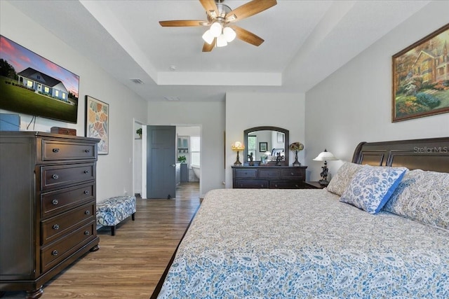 bedroom featuring a tray ceiling, wood finished floors, connected bathroom, and ceiling fan