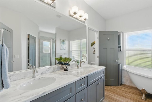 full bath with a stall shower, double vanity, a freestanding bath, and wood finished floors