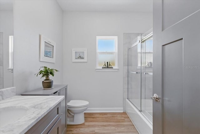 bathroom with wood finished floors, vanity, toilet, enclosed tub / shower combo, and baseboards