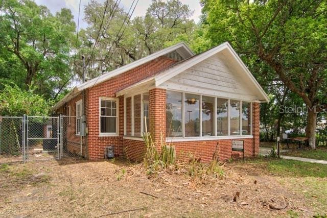 113 NW 11th St Unit 1/2, Gainesville, FL 32601 - view of home's exterior with a gate, a sunroom, brick siding, and fence