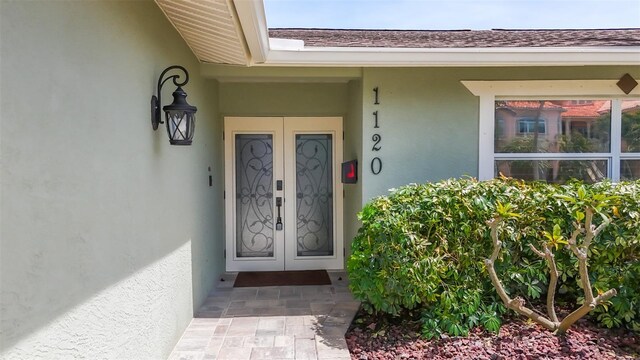 1120 81st St S, Saint Petersburg, FL 33707 - view of exterior entry featuring french doors, stucco siding, and roof with shingles
