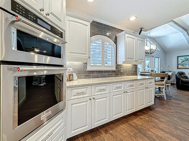 1120 81st St S, Saint Petersburg, FL 33707 - kitchen with stainless steel double oven, vaulted ceiling, white cabinetry, dark wood-style floors, and a chandelier