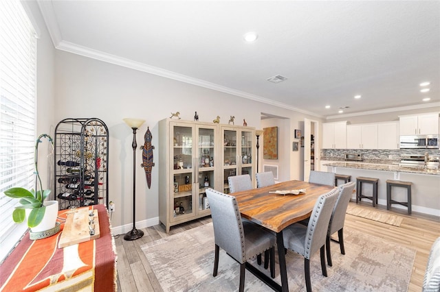 dining area featuring ornamental molding, light wood finished floors, baseboards, recessed lighting, and healthy amount of natural light