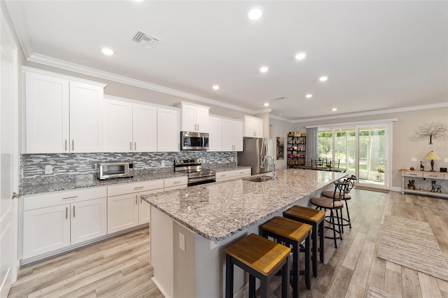 kitchen featuring appliances with stainless steel finishes, an island with sink, a sink, tasteful backsplash, and a breakfast bar