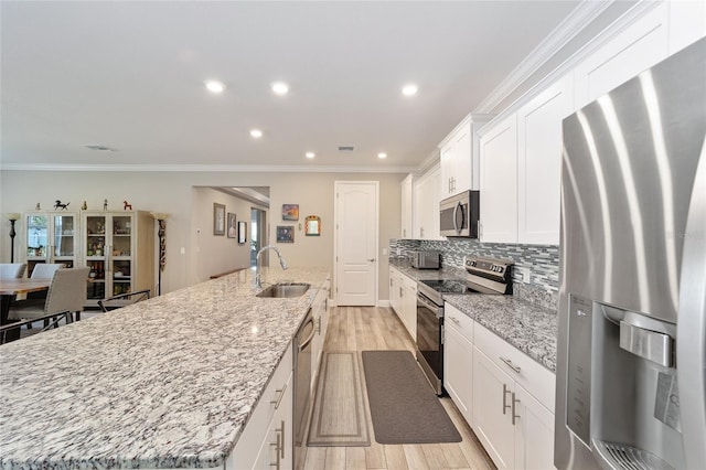 kitchen featuring stainless steel appliances, an island with sink, light wood-style floors, a sink, and white cabinetry