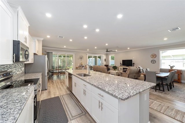kitchen featuring appliances with stainless steel finishes, a sink, ornamental molding, a kitchen island with sink, and white cabinets