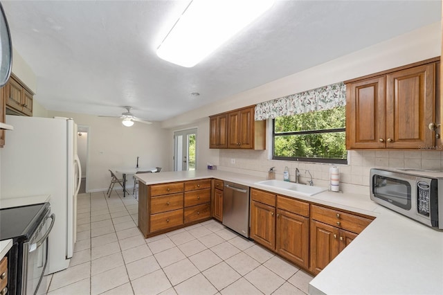 13207 SW Williston Rd, Micanopy, FL 32667 - kitchen with stainless steel appliances, a sink, light tile patterned floors, a peninsula, and brown cabinets