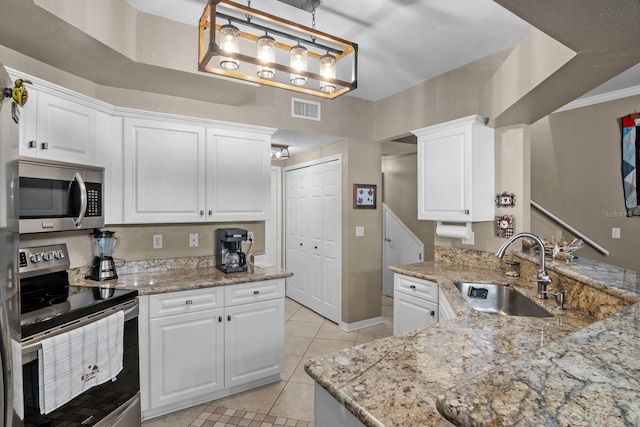 kitchen featuring appliances with stainless steel finishes, a sink, light tile patterned floors, white cabinetry, and light stone counters