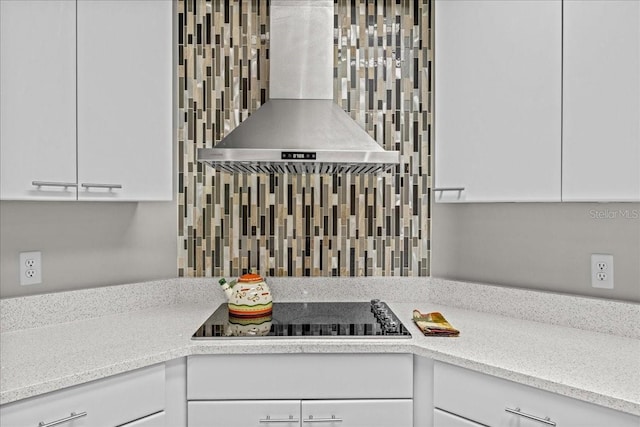 kitchen view of wall chimney exhaust hood, black electric stovetop, white cabinets, and light stone counters