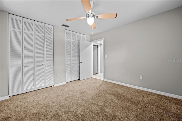 unfurnished bedroom with carpet, two closets, baseboards, and ceiling fan