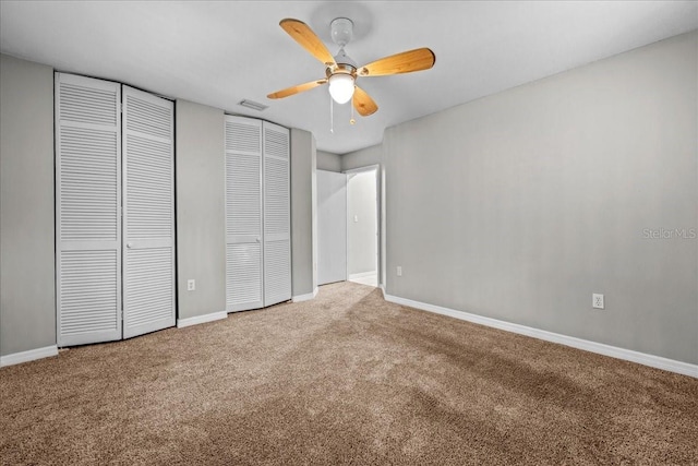 unfurnished bedroom featuring multiple closets, carpet flooring, baseboards, and ceiling fan