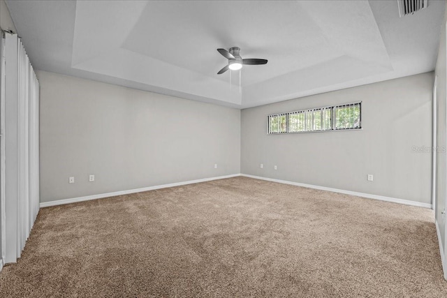 carpeted spare room featuring a tray ceiling, ceiling fan, and baseboards
