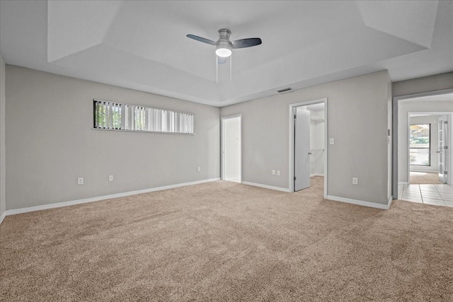 unfurnished bedroom featuring a tray ceiling, light carpet, multiple windows, and a walk in closet