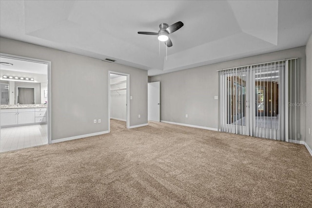 unfurnished bedroom featuring a raised ceiling, carpet floors, baseboards, and ensuite bath