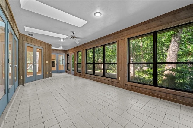 unfurnished sunroom featuring french doors, a skylight, healthy amount of natural light, wood walls, and tile patterned flooring