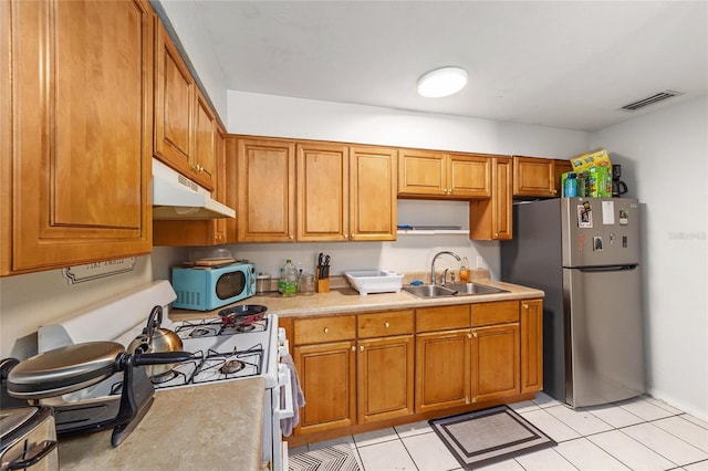 6117 NW 23rd Ter, Gainesville, FL 32653 - kitchen with under cabinet range hood, a sink, freestanding refrigerator, and brown cabinets