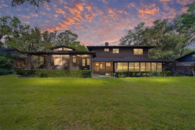 6015 SW 36th Way, Gainesville, FL 32608 - back of house at dusk with a sunroom, a yard, a chimney, and brick siding