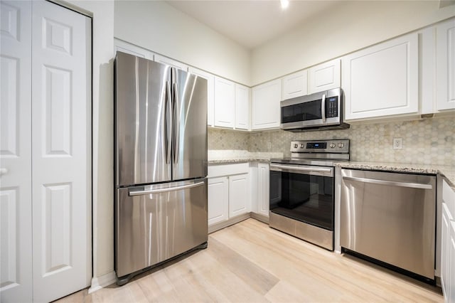4850 SW 91st Ter Unit P201, Gainesville, FL 32608 - kitchen featuring appliances with stainless steel finishes, white cabinetry, decorative backsplash, light stone counters, and light wood-type flooring