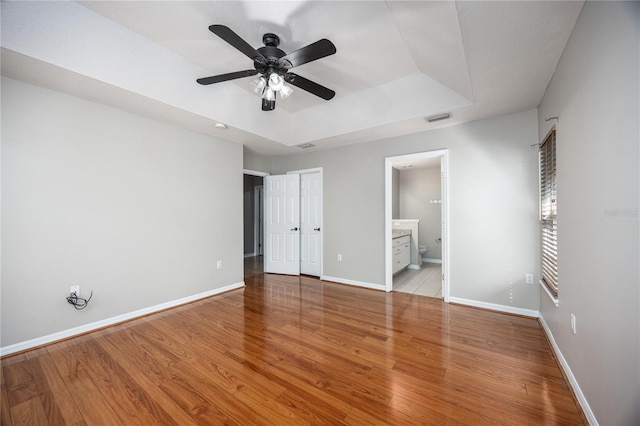 8103 SW 71st Ln, Gainesville, FL 32608 - unfurnished bedroom featuring a raised ceiling, baseboards, light wood-style floors, ensuite bathroom, and ceiling fan