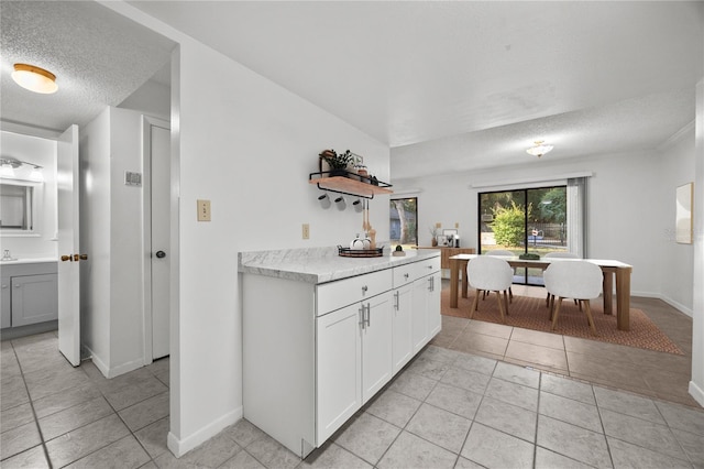 3026 NW 28th Cir, Gainesville, FL 32605 - kitchen featuring a textured ceiling, light tile patterned floors, light countertops, baseboards, and white cabinetry