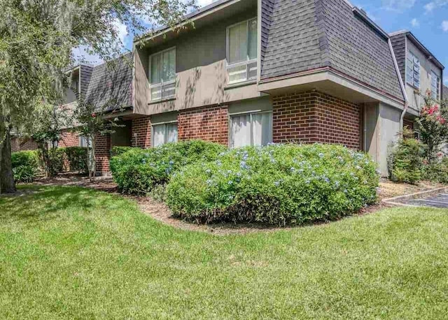 1700 SW 16th Ct Unit J22, Gainesville, FL 32608 - view of side of home with brick siding, mansard roof, a shingled roof, and a yard