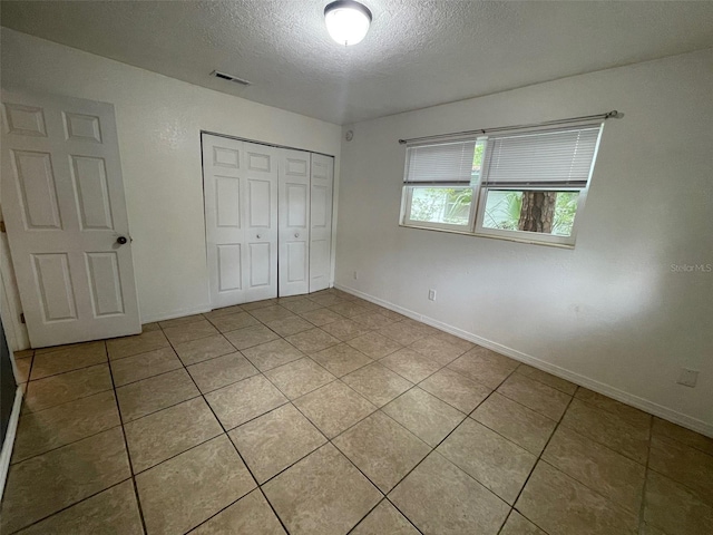 1702 NE 15th Ter, Gainesville, FL 32609 - unfurnished bedroom featuring a textured ceiling, light tile patterned floors, a closet, and baseboards