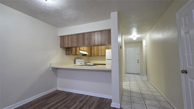 2635 SW 35th Pl Unit 1705, Gainesville, FL 32608 - kitchen featuring white appliances, brown cabinetry, light countertops, under cabinet range hood, and baseboards