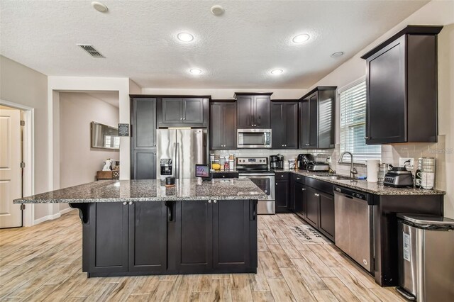 13201 Orca Sound Dr, Riverview, FL 33579 - kitchen featuring appliances with stainless steel finishes, a sink, a center island, dark stone counters, and a textured ceiling