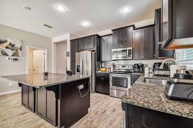 13201 Orca Sound Dr, Riverview, FL 33579 - kitchen with stainless steel appliances, dark stone counters, wood finish floors, a kitchen island, and tasteful backsplash