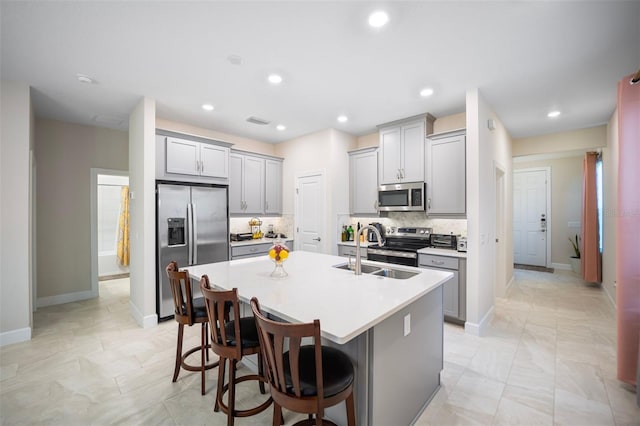 1192 Via Galuppi St, Poinciana, FL 34759 - kitchen featuring appliances with stainless steel finishes, a sink, gray cabinets, a kitchen island with sink, and backsplash