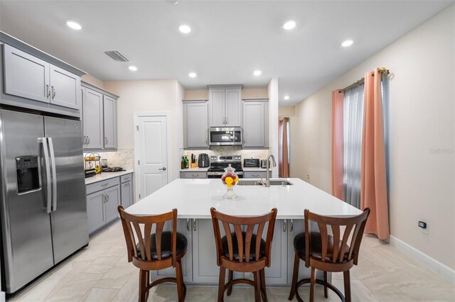 1192 Via Galuppi St, Poinciana, FL 34759 - kitchen with stainless steel appliances, gray cabinets, decorative backsplash, light countertops, and an island with sink