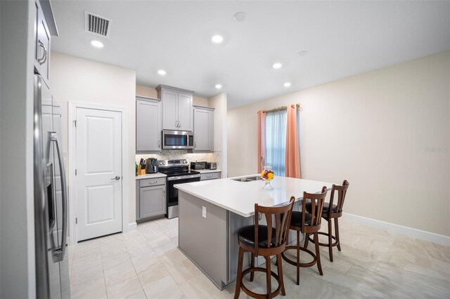 1192 Via Galuppi St, Poinciana, FL 34759 - kitchen featuring appliances with stainless steel finishes, gray cabinets, a center island with sink, a breakfast bar area, and light countertops