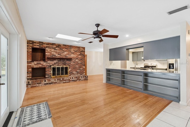 2626 NW 36th Pl, Gainesville, FL 32605 - unfurnished living room with ceiling fan, a skylight, a fireplace, light wood finished floors, and recessed lighting