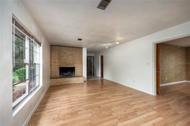 2147 NW 7th Pl, Gainesville, FL 32603 - unfurnished living room with light wood-style flooring, a brick fireplace, and track lighting