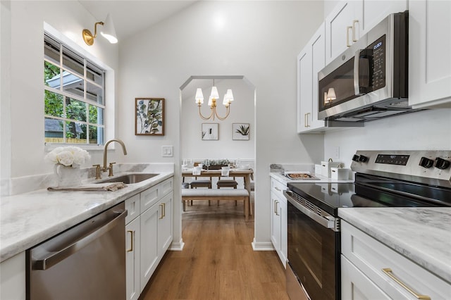 10943 NW 34th Pl, Gainesville, FL 32606 - kitchen with stainless steel appliances, wood finished floors, white cabinetry, arched walkways, and a chandelier