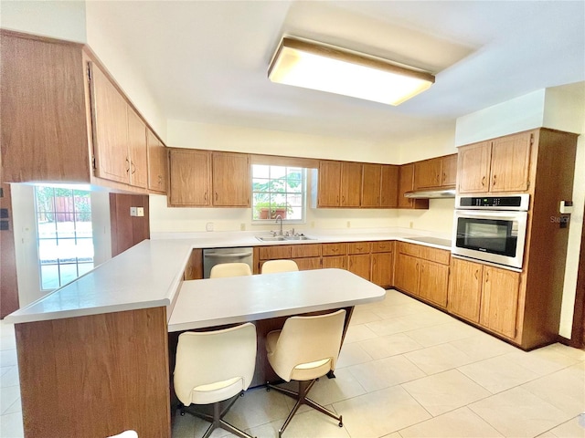 2268 NW 17th Ave, Gainesville, FL 32605 - kitchen with stainless steel appliances, a peninsula, a kitchen breakfast bar, light countertops, and under cabinet range hood
